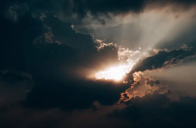 A single beam of sunlight breaking through a wall of dark storm clouds.